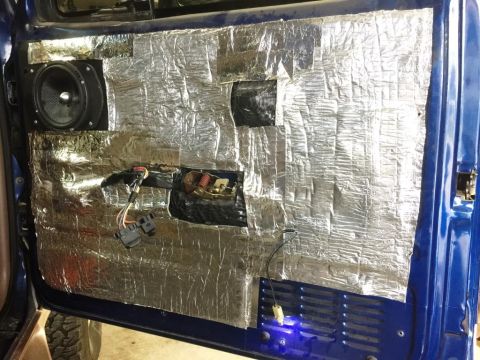 1996 Ford Bronco - The interior of a blue vehicle's door panel is covered in soundproofing material, revealing a speaker and wiring.
