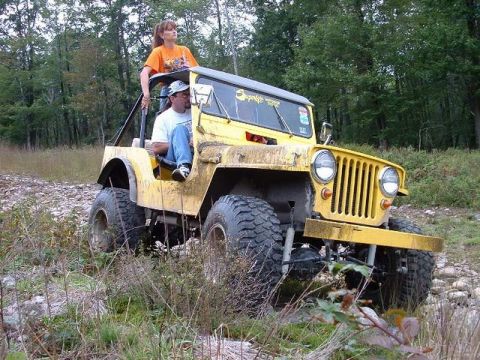 1978 Ford Bronco - Yellow Jeep CJ-5 navigating rough terrain with two occupants.