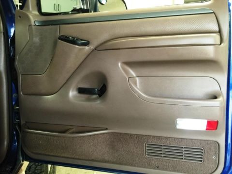 1996 Ford Bronco - Interior door panel of a 1996 Ford Bronco, brown upholstery, a speaker grille, and a storage pocket.
