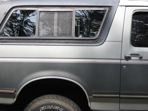 Side view of a two-tone SUV with a camper shell, showing the rear window and door