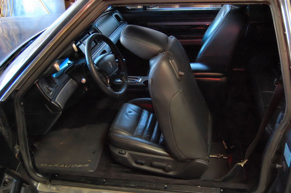 Interior shot of a car with black leather seats and a steering wheel. Floor mat says 'Marauder'