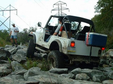 1978 Ford Bronco - Jeep CJ-7 tackling a difficult rocky terrain, with a cooler mounted on the back.