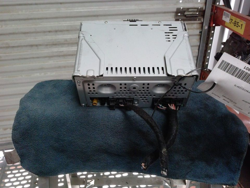 Removed silver Ford Taurus radio module with wiring harnesses, shown rear side up on a blue towel