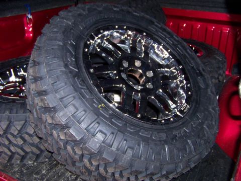 2005 Ford F-150 - Aftermarket chrome wheels and mud tires are stacked in the bed of a red truck.