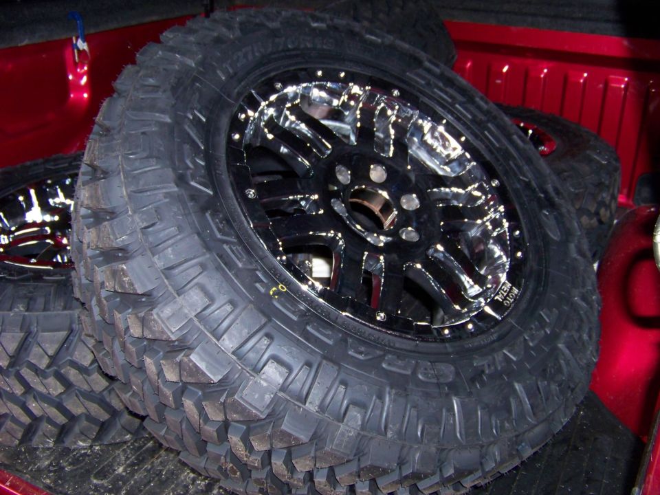 Aftermarket chrome wheels and mud tires stacked in a red truck bed