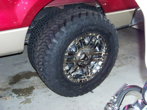 2005 Ford F-150 - Close-up of the dual rear wheels and chrome rims on a red and tan truck, showing off the off-road tires.