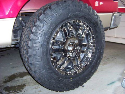2005 Ford F-150 - Close-up of a red and tan truck's wheel and tire, a chrome rim and off-road tire tread.
