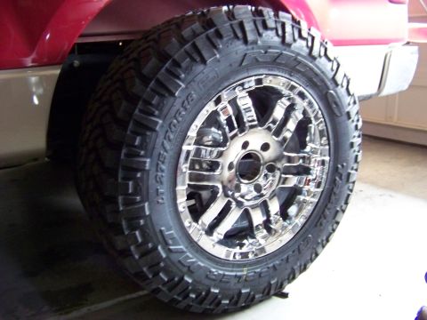 2005 Ford F-150 - Close-up of a chrome wheel and tire mounted on the side of a red vehicle.