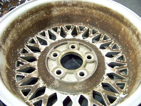 1999 Mercury Grand Marquis - This is a close-up of a dirty alloy wheel with a mesh pattern. It has five lug nut holes and text indicating it was made in Italy.