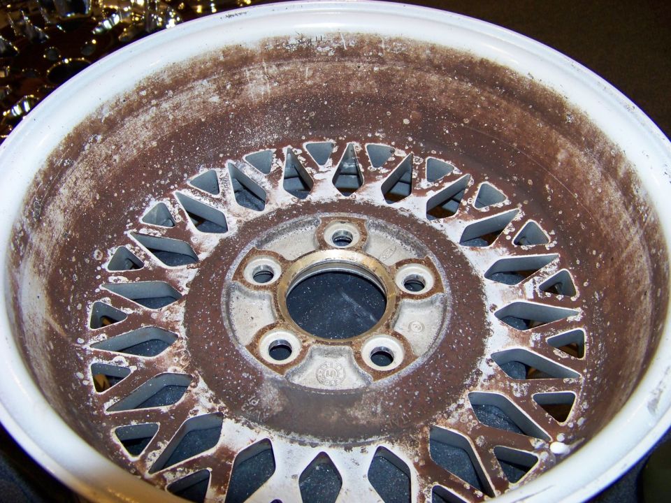 Close-up of a rusty, old aluminum wheel with a complex spoke pattern