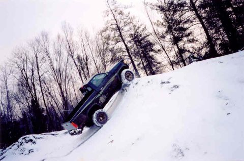 1978 Ford Bronco - A dark pickup truck navigates a steep, snow-covered hill with trees in the background.