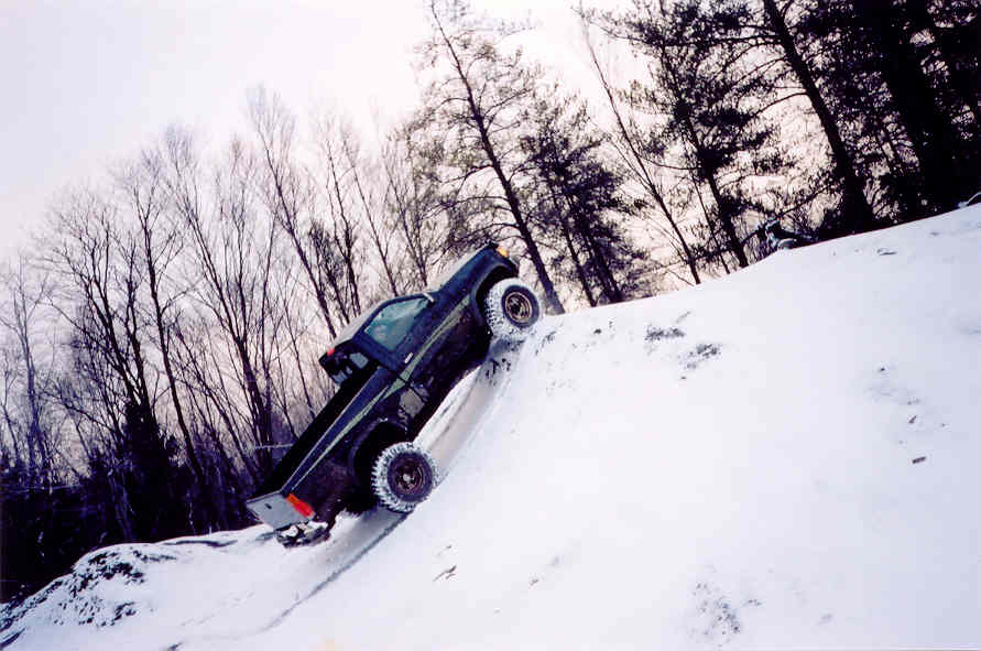 Dark pickup truck on snowy incline, tires digging into snow