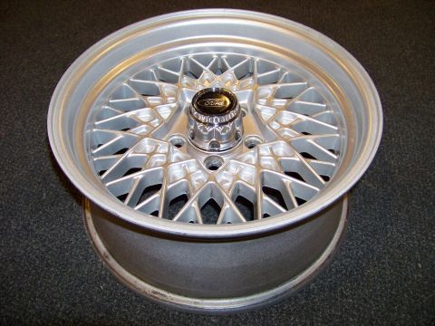 1999 Mercury Grand Marquis - Silver mesh-style alloy wheel with a chrome Ford center cap photographed on a dark floor.