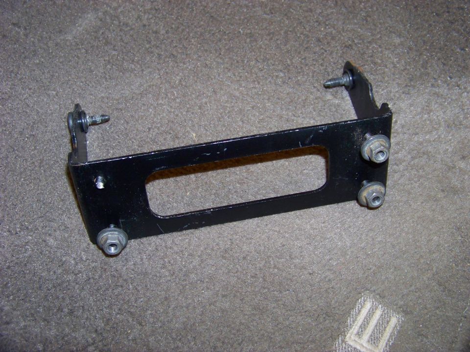 Black metal bracket with four bolts, resting on carpet
