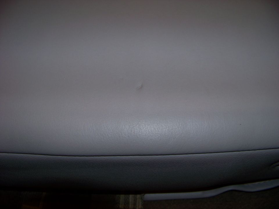 Gray leather armrest with a small scuff mark, showing the bottom edge of the seat cushion