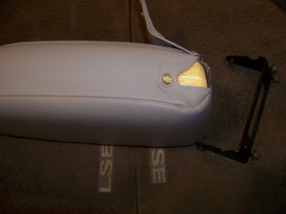 Gray car armrest with yellow foam exposed, next to a black metal mounting bracket. 'LSE' and 'SE' are visible on the carpet