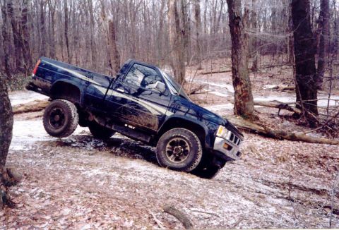 1978 Ford Bronco - A dark blue pickup truck navigates a challenging wooded trail with snow on the ground.