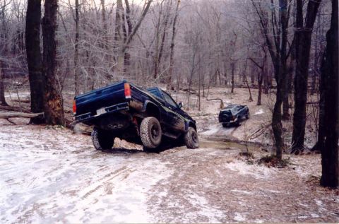 1978 Ford Bronco - Two trucks are shown off-roading on a winter trail in a wooded area.
