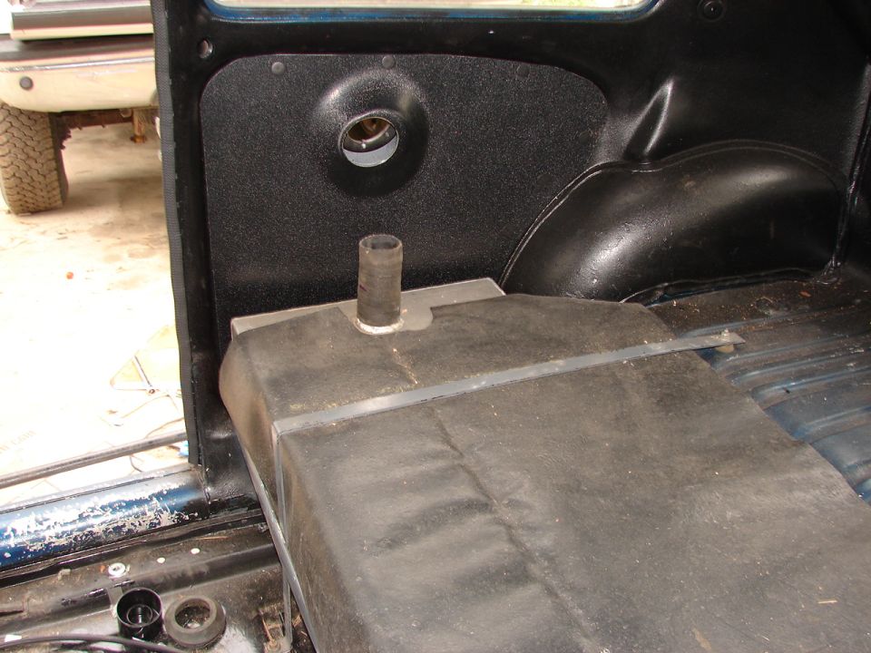 Interior view of a vehicle showing a fuel tank and black plastic panel with a circular opening