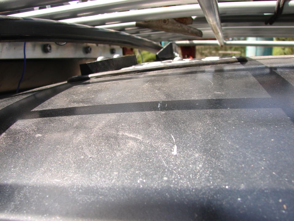 Black roof rack with metal bars and wooden support over a dusty car roof