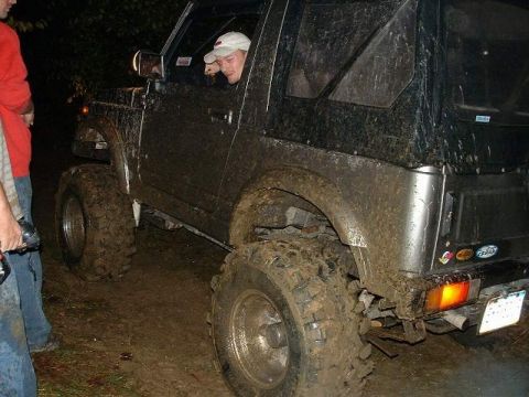 1978 Ford Bronco - A muddy off-road vehicle is driven by a person wearing a white cap.