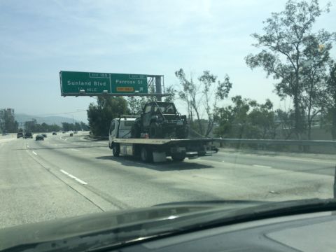 1987 Suzuki Samurai - An off-road vehicle is transported on a flatbed truck along a highway under a clear sky.