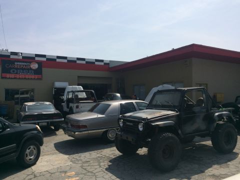 1987 Suzuki Samurai - Several vehicles are parked outside a repair shop, including a modified off-road vehicle.