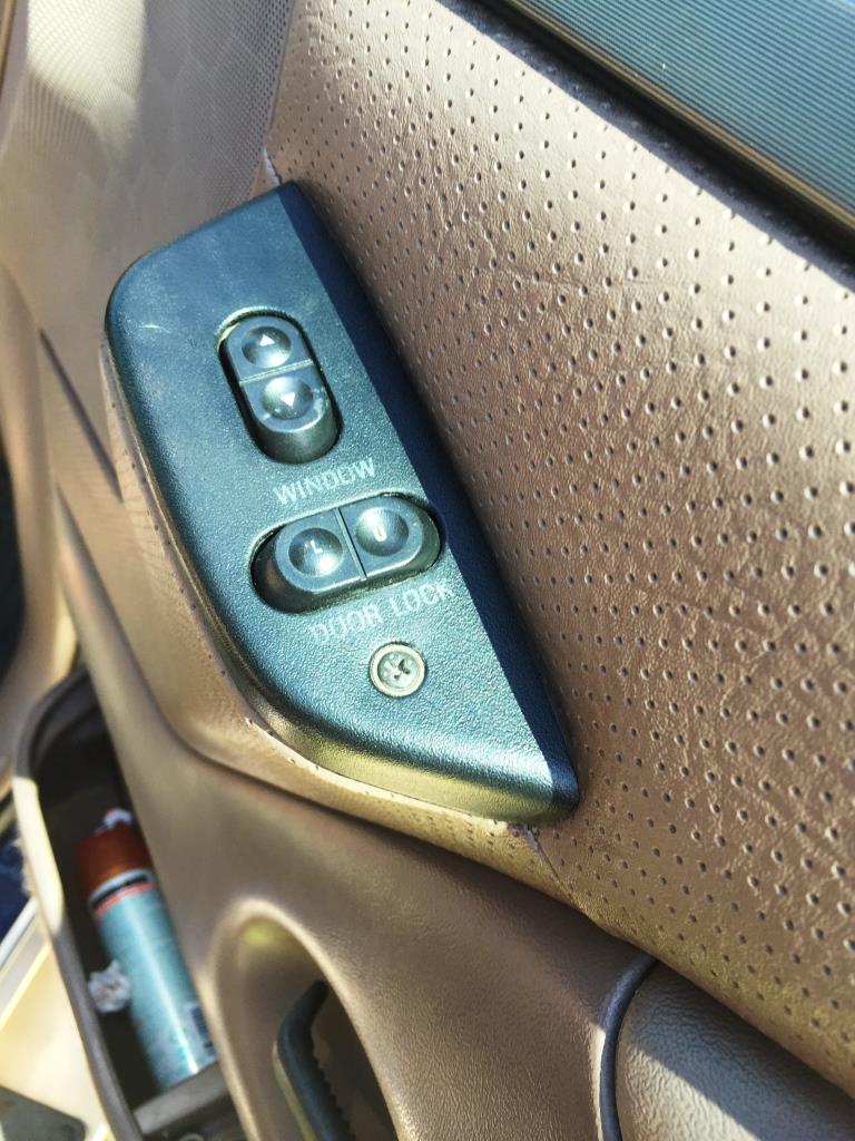 1996 Ford Bronco interior door panel with window and door lock switches. Perforated tan upholstery visible