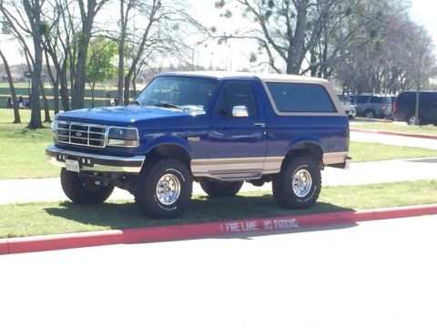 1996 Ford Bronco - This lifted blue Ford Bronco with a tan top is parked on grass near a fire lane.