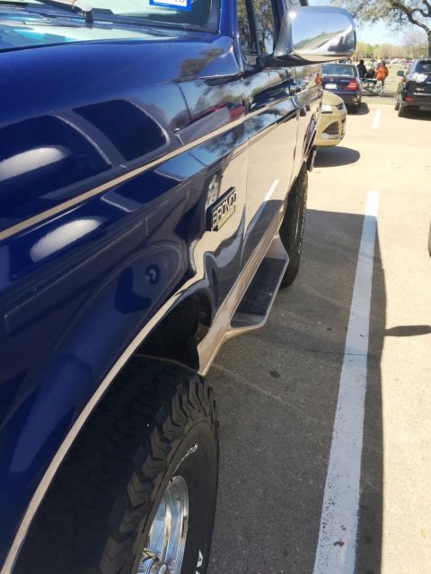 1996 Ford Bronco - This blue 1996 Ford Bronco features tan trim and prominent running boards, viewed from the side.