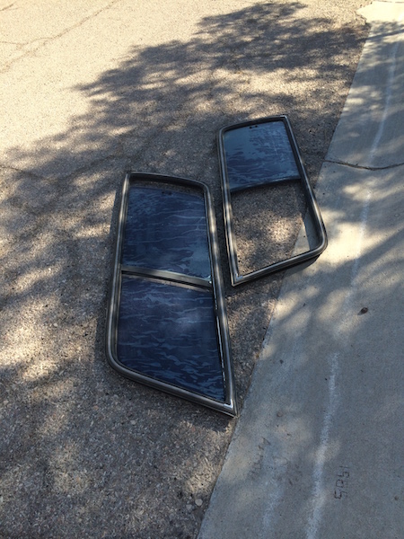 1981 Ford Bronco - Two car door windows with dark tint and chrome trim are placed on asphalt, casting shadows.