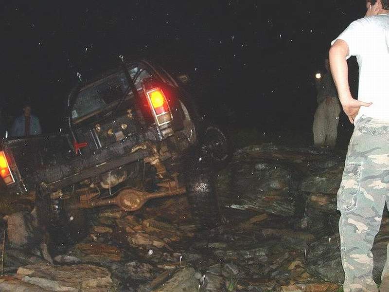 Off-road vehicle tilted on rocks at night, rear view showing taillights and suspension