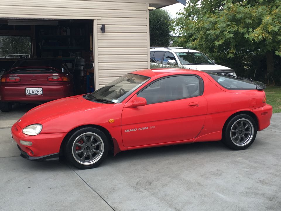 Red Mazda MX-3 Quad Cam V6 coupe parked outside a garage with another red car