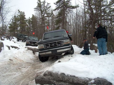 1993 Ford Bronco - Several off-road vehicles tackle a challenging snowy terrain, with the lead Bronco at a difficult angle.