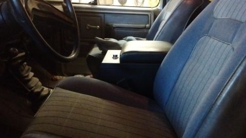1985 Ford Bronco - The interior of a 1985 Ford Bronco features blue striped cloth seats, a central armrest, and a floor-mounted gear shifter.