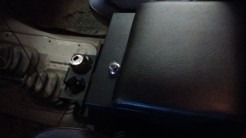 1985 Ford Bronco - A can sits in the cup holder of a vehicle's center console, next to a button on the armrest.