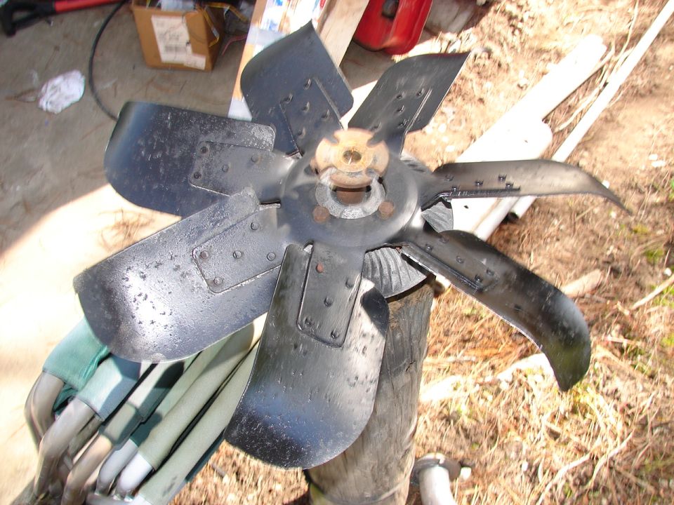 Black metal engine cooling fan with six blades, resting on a wooden post