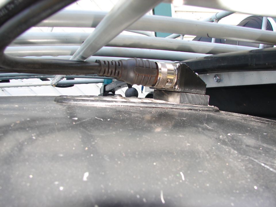 Close-up of a roof rack mount with a cable connector attached to a dark surface