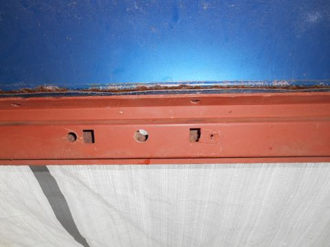 1972 Ford Bronco - Close-up of a rusted seam between blue and red painted metal car parts.