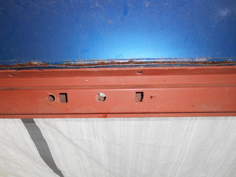 Close-up of rusted seam between blue and red painted metal car parts