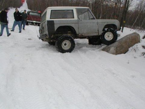 1993 Ford Bronco - A group of people and vehicles are in a snowy area, with one vehicle attempting to drive over a large rock.