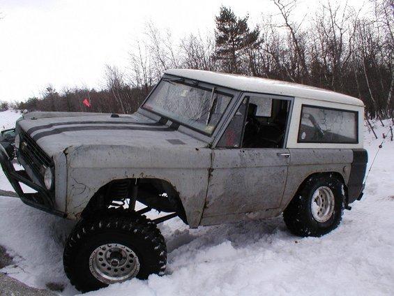 Gray Ford Bronco with black racing stripes, lifted suspension, and large tires in the snow