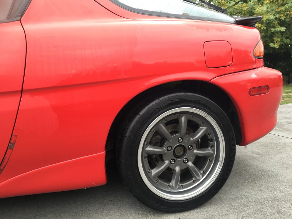 Red 1993 Mazda MX-3 rear quarter panel and wheel with aftermarket gray rims