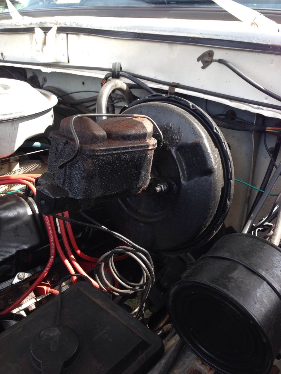 Engine bay with brake booster, master cylinder, and wiring. White vehicle exterior visible