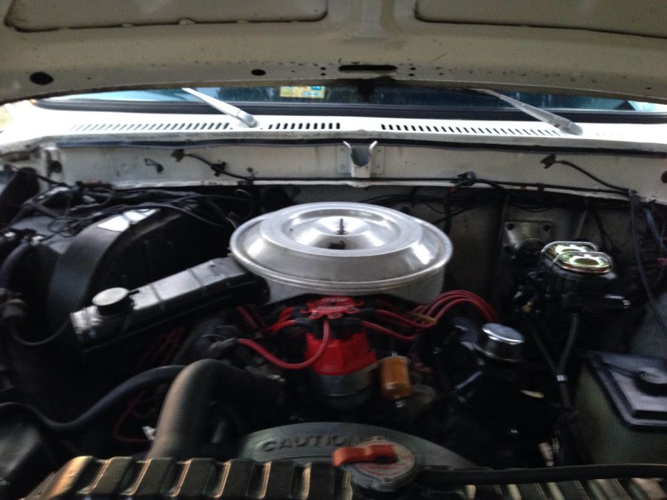 White vehicle engine bay with a chrome air cleaner, red spark plug wires, and a radiator