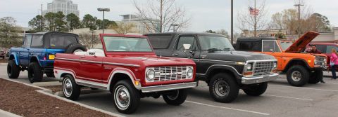1979 Ford Bronco - A line of Ford Broncos, including a red convertible and a black model, are parked in a lot.