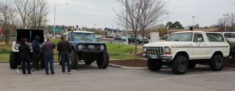 1979 Ford Bronco - A white 1979 Ford Bronco is parked next to a blue off-road vehicle, with people gathered around another vehicle with its hood open.
