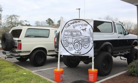 1979 Ford Bronco - Two Ford Broncos, a white first-gen and a black/white lifted second-gen, are parked together with a club banner.