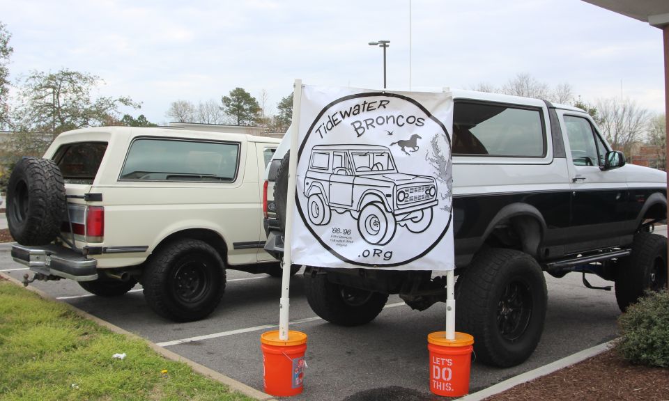Two Ford Broncos parked, one white with spare tire on back, one black and white lifted. Banner reads 'Tidewater Broncos .Org'