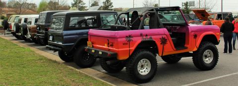 1979 Ford Bronco - Several Ford Broncos are parked in a row, with the closest one a vibrant pink and orange sunset graphic.